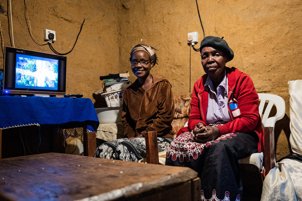 Two women watching TV with an off-grid connection through a Solar Home System appliance.